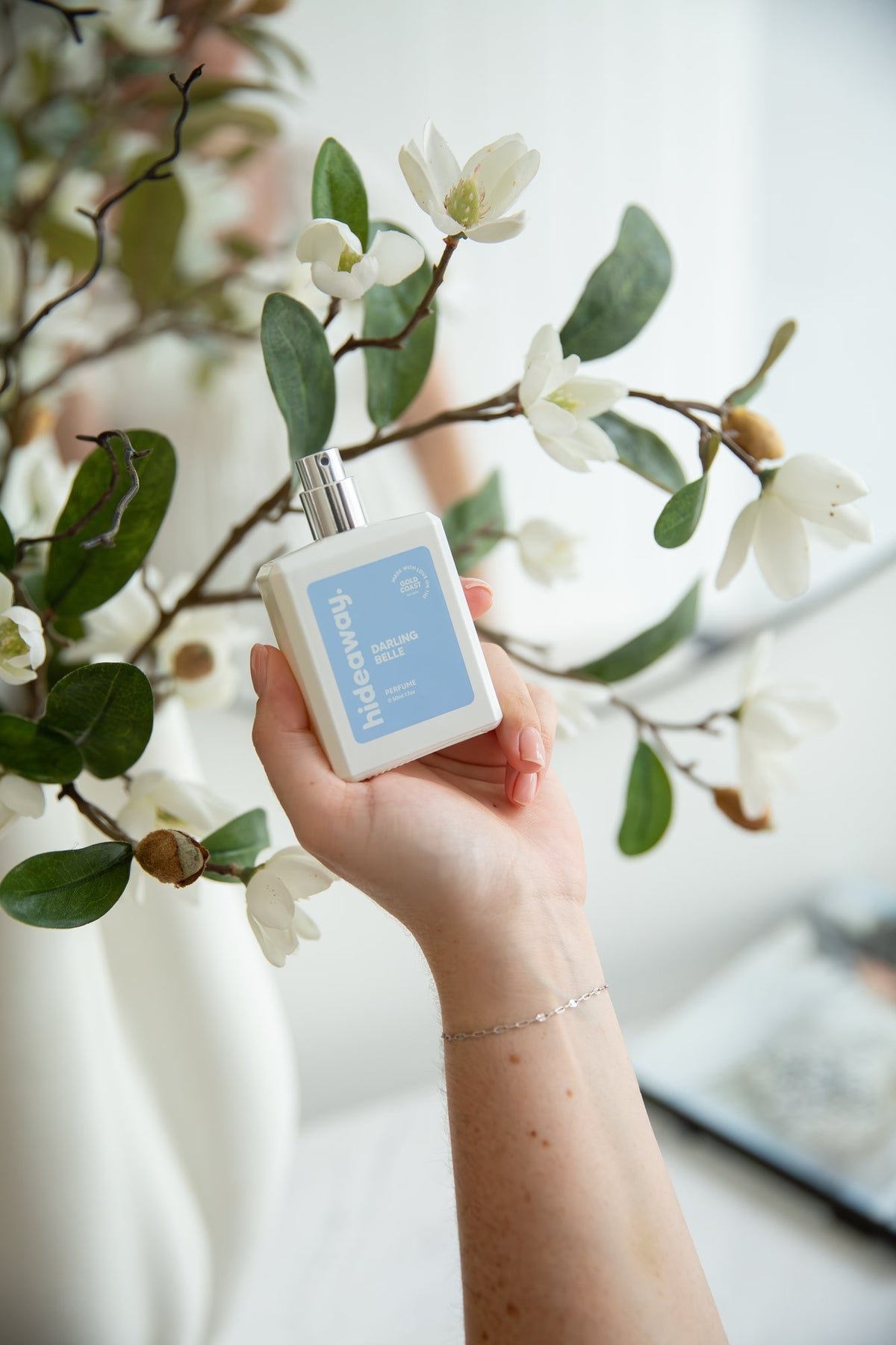 Holding a hideaway. perfume in front of magnolia flowers