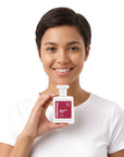 A smiling woman holding Hideaway. Delicate Rose perfume