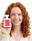 A smiling woman holding Hideaway. Floral Frenzy perfume