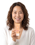 A smiling woman holding Hideaway. Aurora Rouge mini hair mask