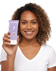 A smiling woman holding Hideaway. Black Essence mini exfoliating body scrub