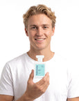 A smiling man holding Hideaway. Ocean Blue perfume