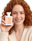 A smiling woman holding Hideaway. Peachy Nights perfume