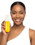 A smiling woman holding Hideaway. Pineapple Coconut body mist