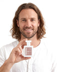 A smiling man holding Hideaway. Sandalwood Grove perfume