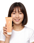A smiling woman holding Hideaway. Vanilla Caramel hair mask