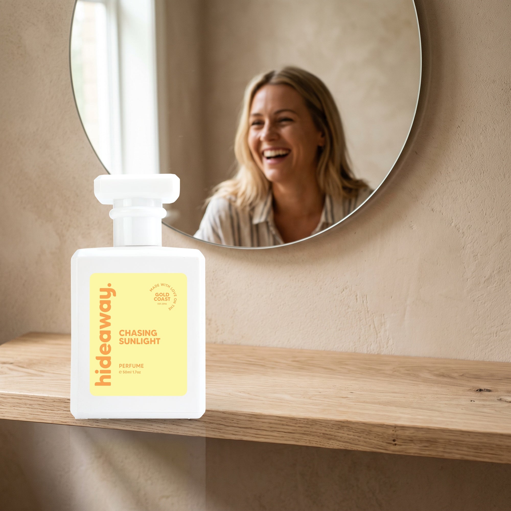 hideaway. Chasing Sunlight perfume 50ml bottle on an oak shelf below a round mirror