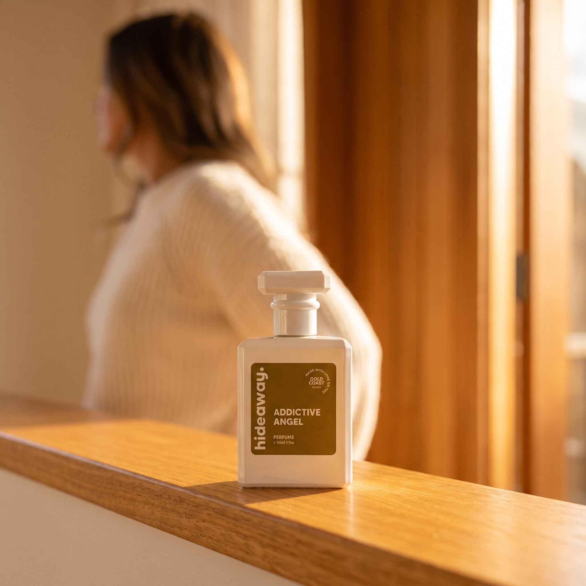 hideaway. Addictive Angel perfume 50ml bottle on a timber sill in warm afternoon light