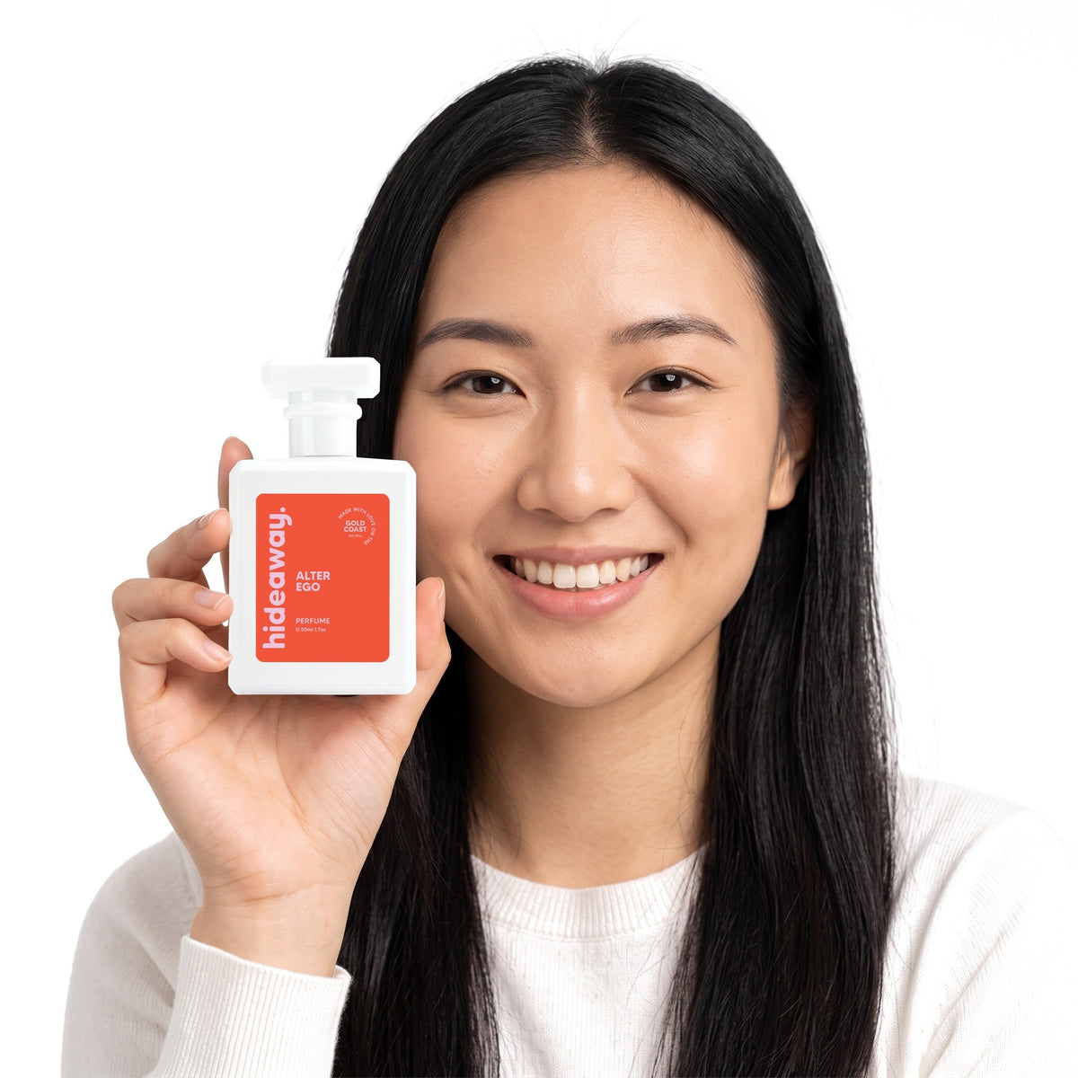 A smiling woman holding Hideaway. Alter Ego perfume