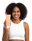 A smiling woman holding Hideaway. Black Essence hair mask