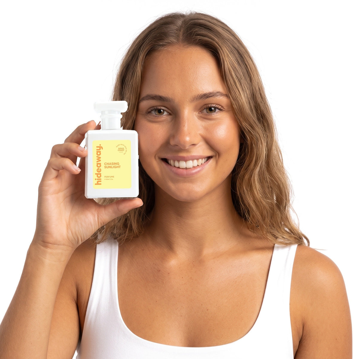 A smiling woman holding Hideaway. Chasing Sunlight perfume