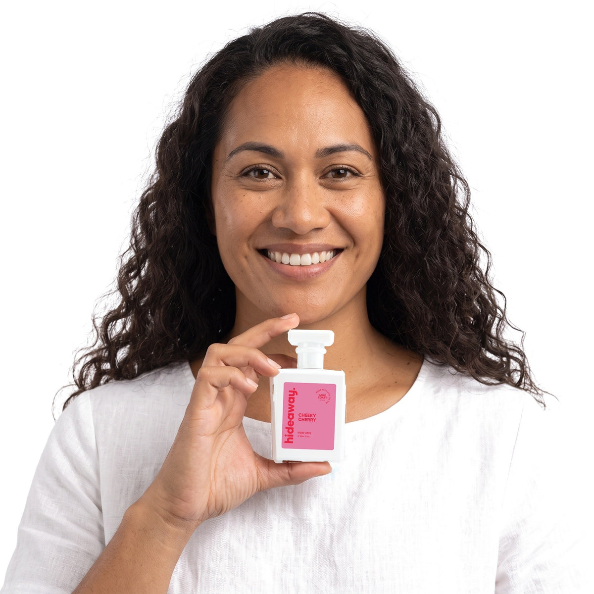 A smiling woman holding Hideaway. Cheeky Cherry perfume