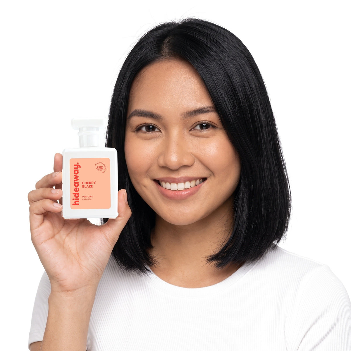 A smiling woman holding Hideaway. Cherry Blaze perfume