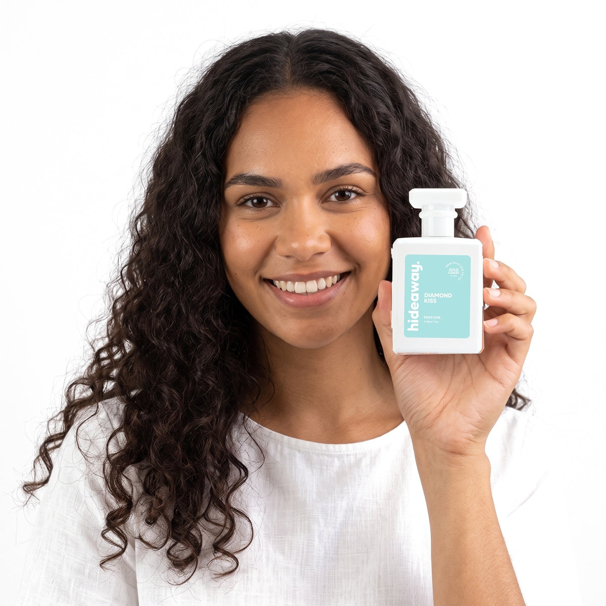 A smiling woman holding Hideaway. Diamond Kiss perfume