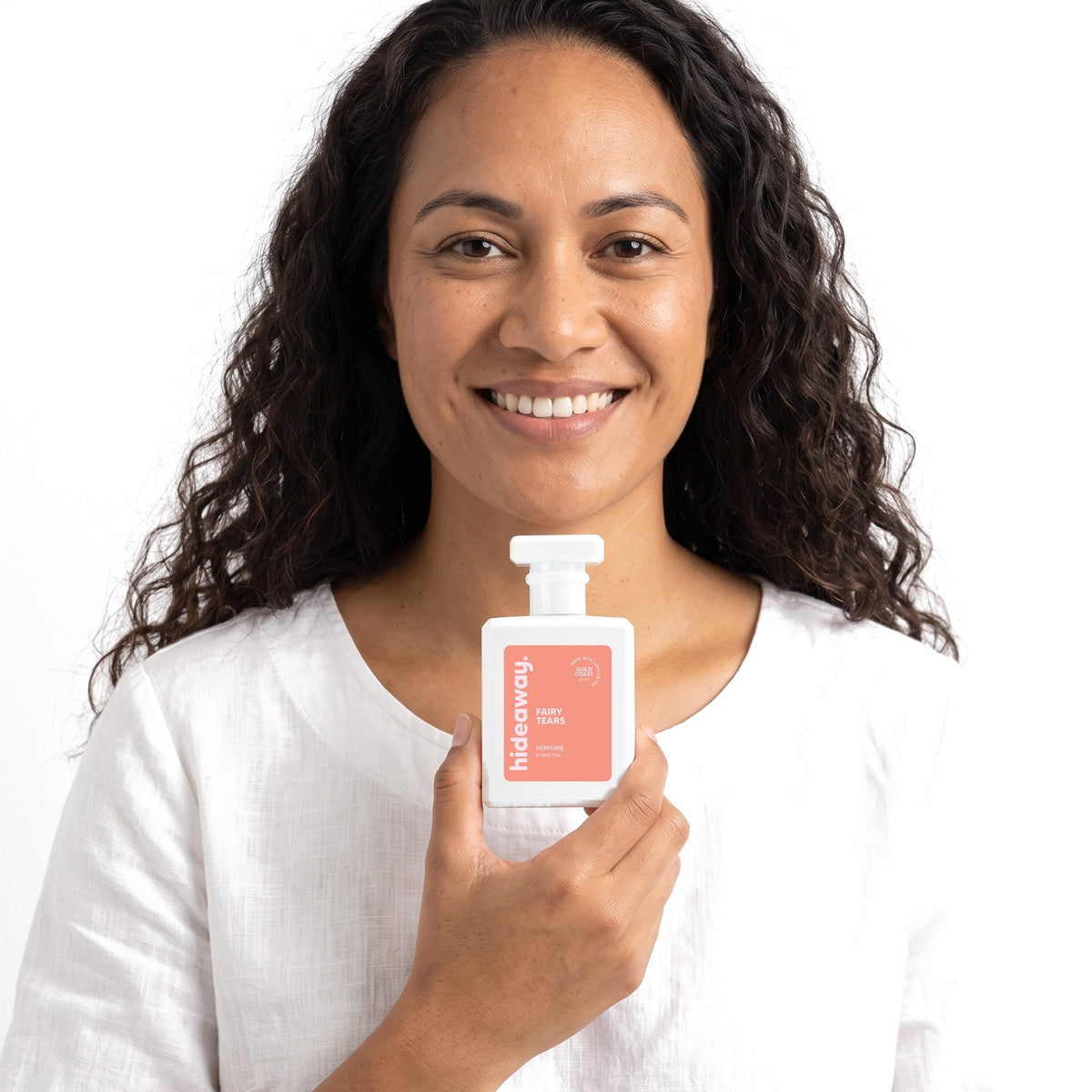A smiling woman holding Hideaway. Fairy Tears perfume