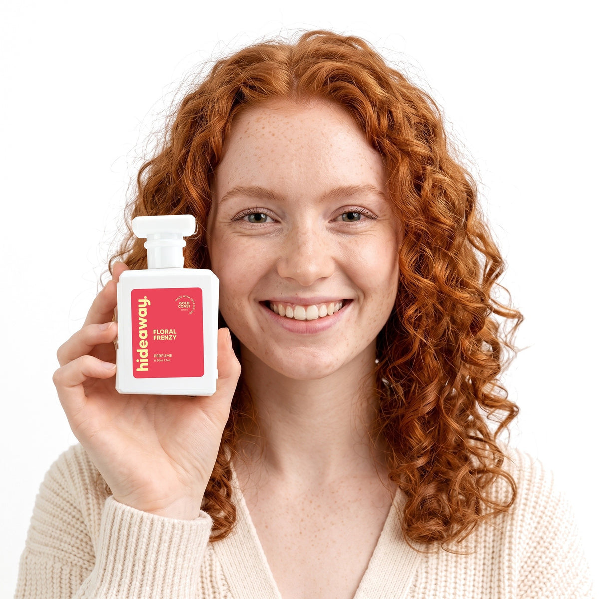 A smiling woman holding Hideaway. Floral Frenzy perfume