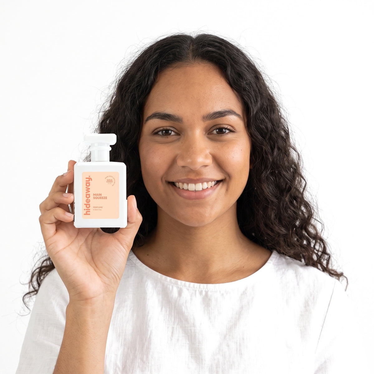A smiling woman holding Hideaway. Main Squeeze perfume