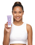 A smiling woman holding Hideaway. Aurora Rouge mini exfoliating body scrub