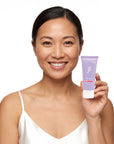 A smiling woman holding Hideaway. Aurora Rouge mini body wash