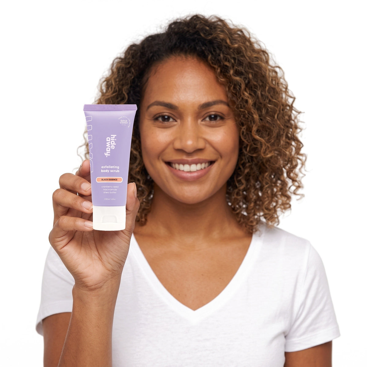 A smiling woman holding Hideaway. Black Essence mini exfoliating body scrub
