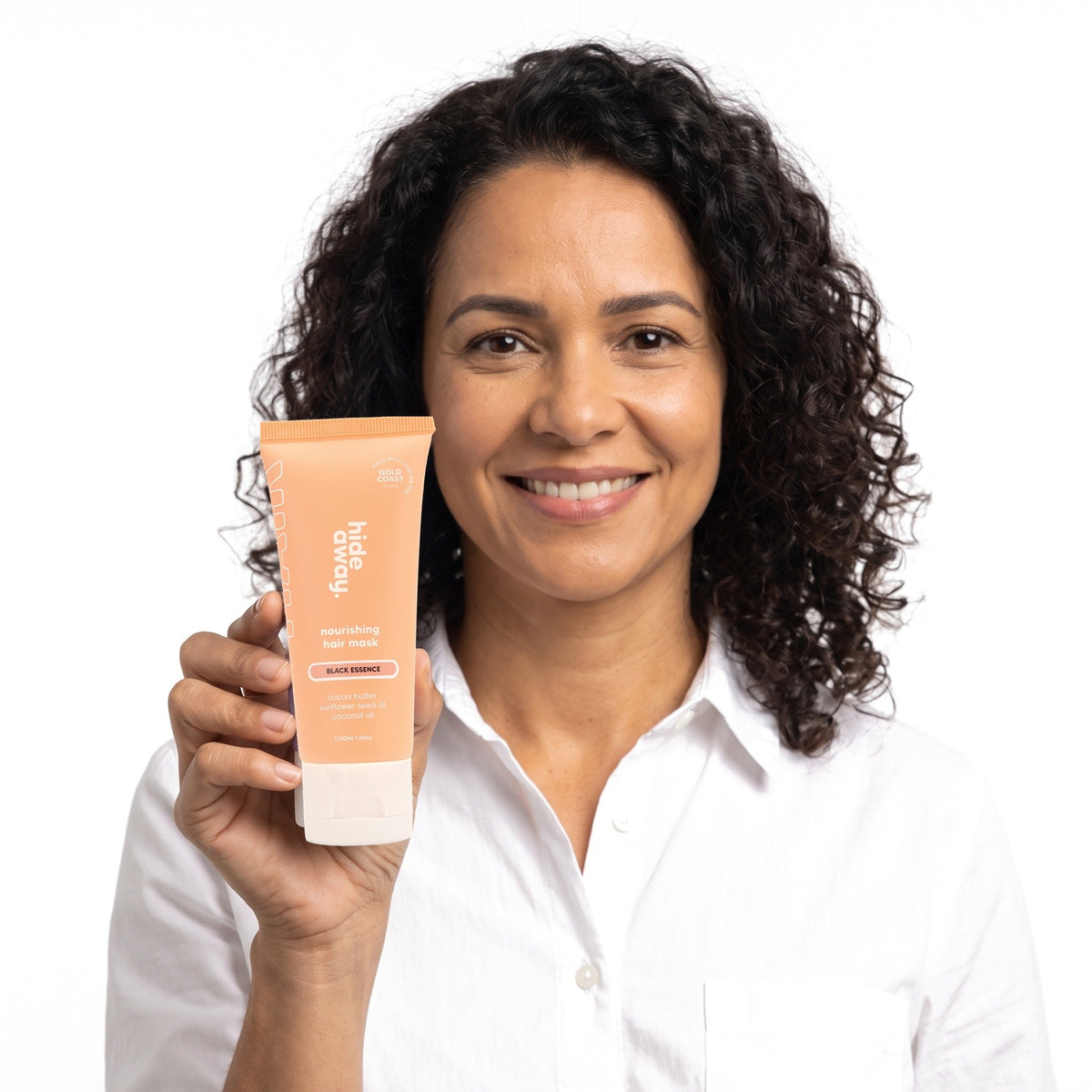 A smiling woman holding Hideaway. Black Essence mini hair mask