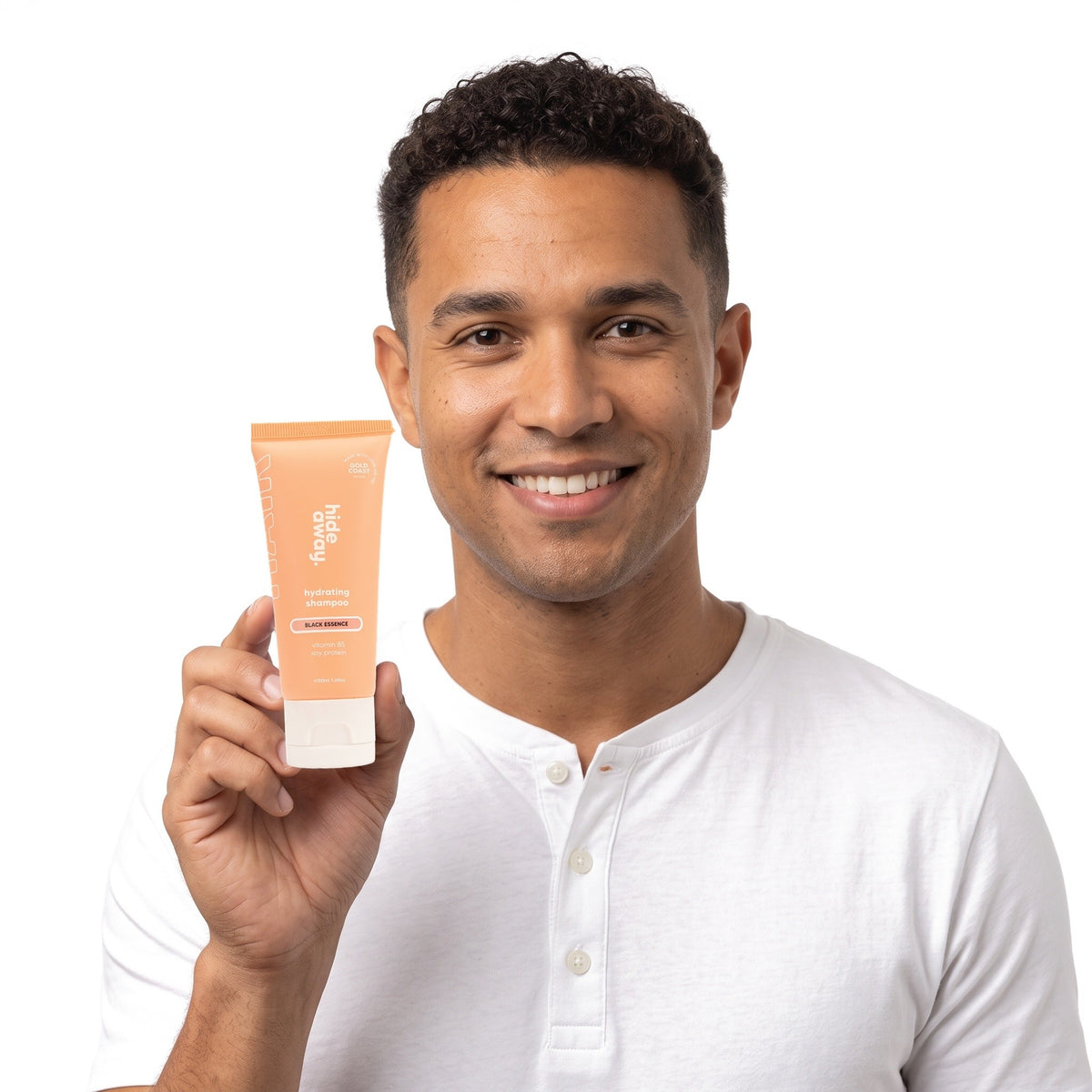 A smiling man holding Hideaway. Black Essence mini shampoo
