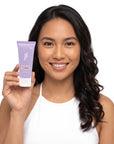 A smiling woman holding Hideaway. Black Essence mini shower mousse