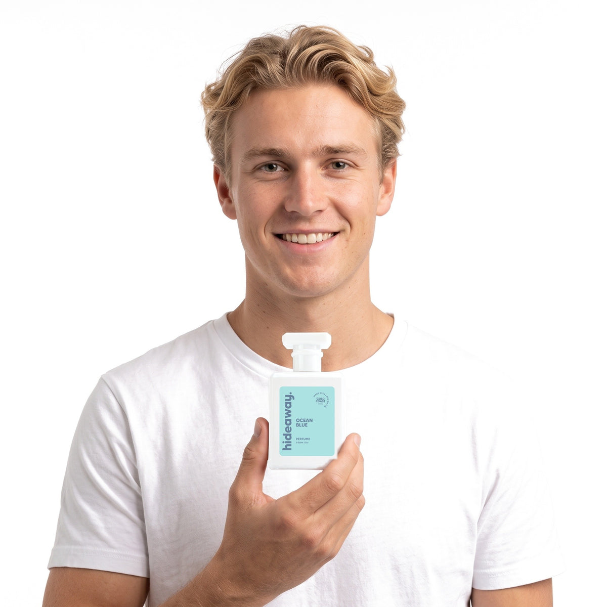 A smiling man holding Hideaway. Ocean Blue perfume