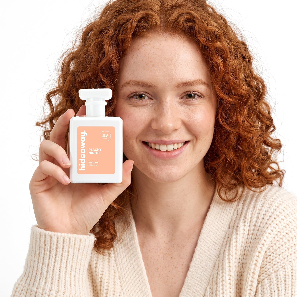 A smiling woman holding Hideaway. Peachy Nights perfume