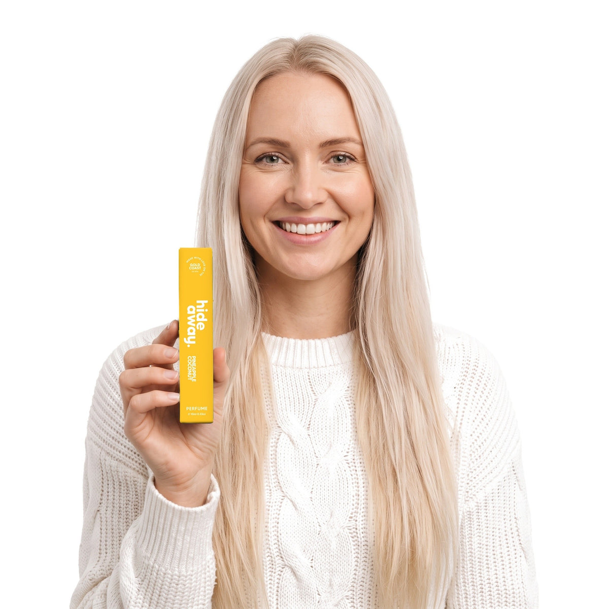 A smiling woman holding the Hideaway. Pineapple Coconut 10ml perfume box