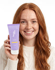 A smiling woman holding Hideaway. Pineapple Coconut exfoliating body scrub
