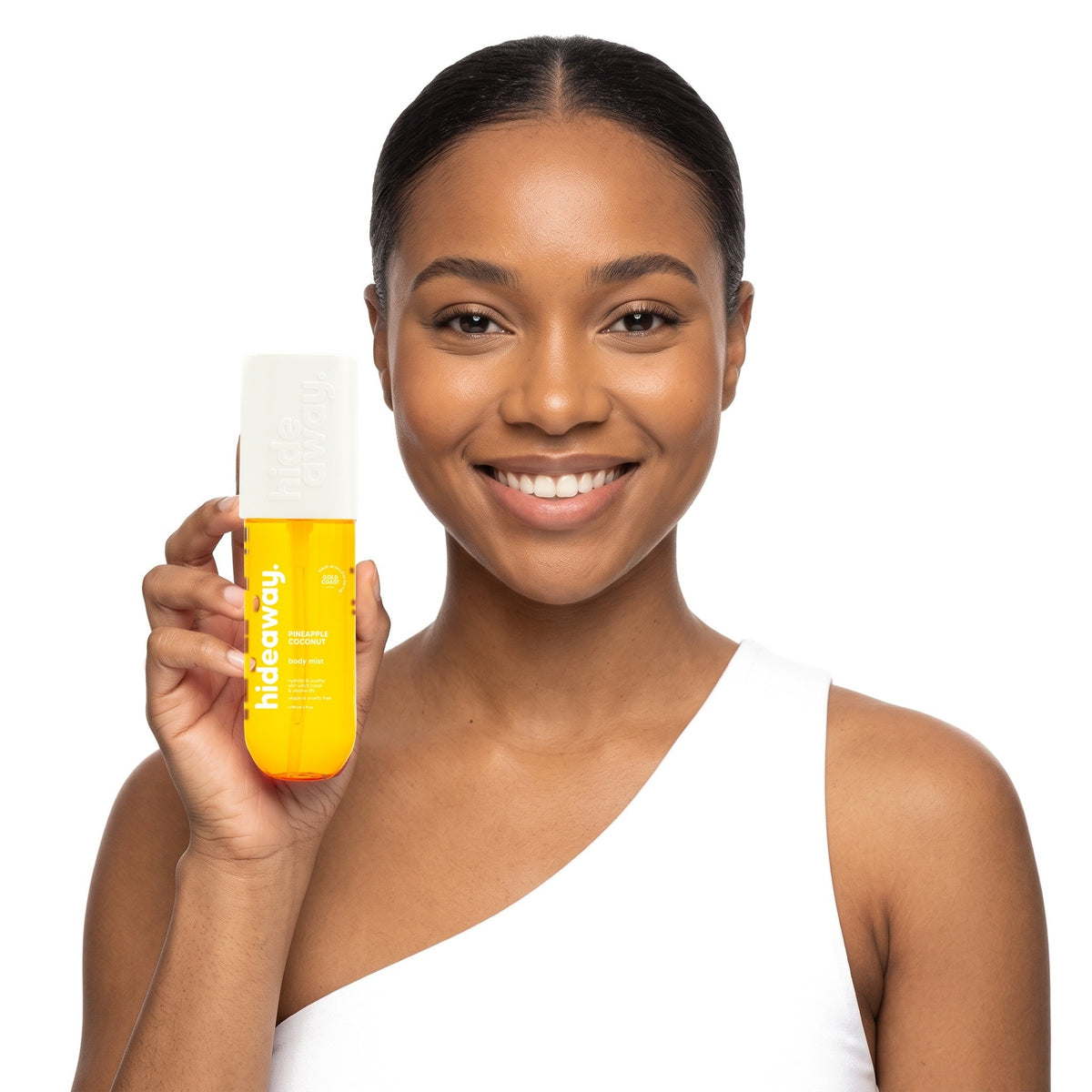 A smiling woman holding Hideaway. Pineapple Coconut body mist