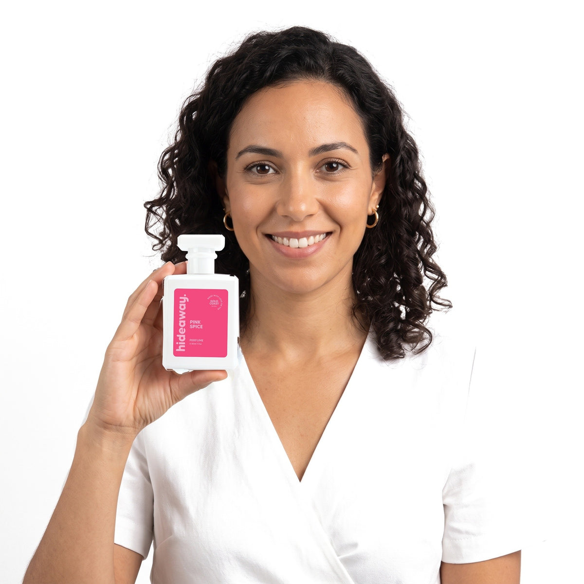 A smiling woman holding Hideaway. Pink Spice perfume