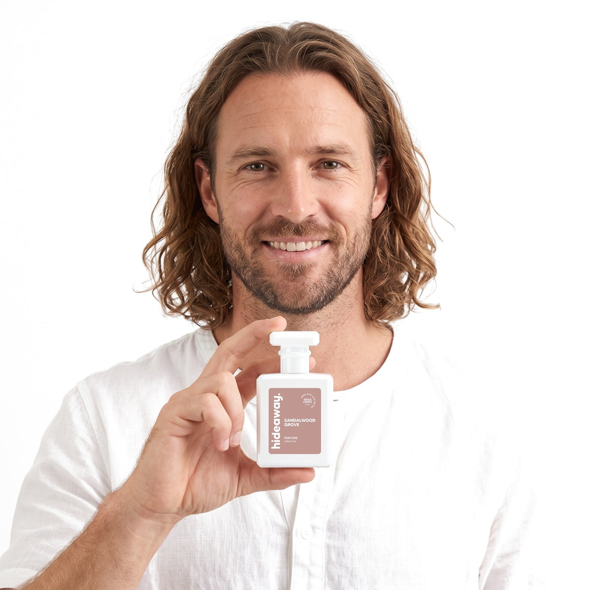 A smiling man holding Hideaway. Sandalwood Grove perfume