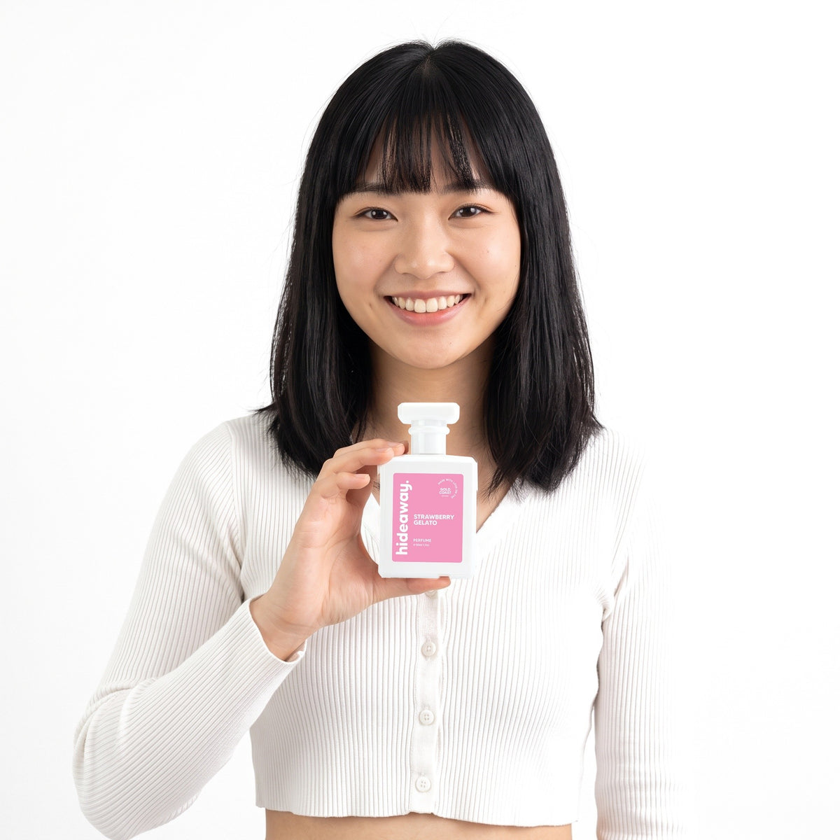 A smiling woman holding Hideaway. Strawberry Gelato perfume