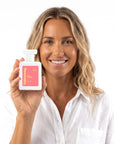 A smiling woman holding Hideaway. Sun Kissed perfume