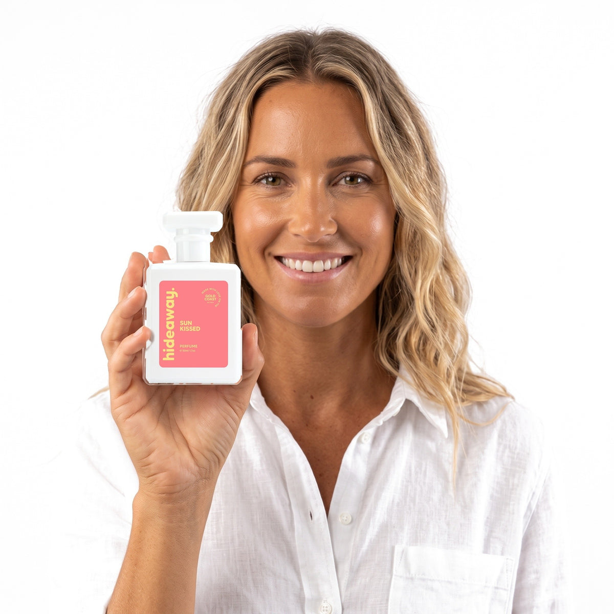 A smiling woman holding Hideaway. Sun Kissed perfume