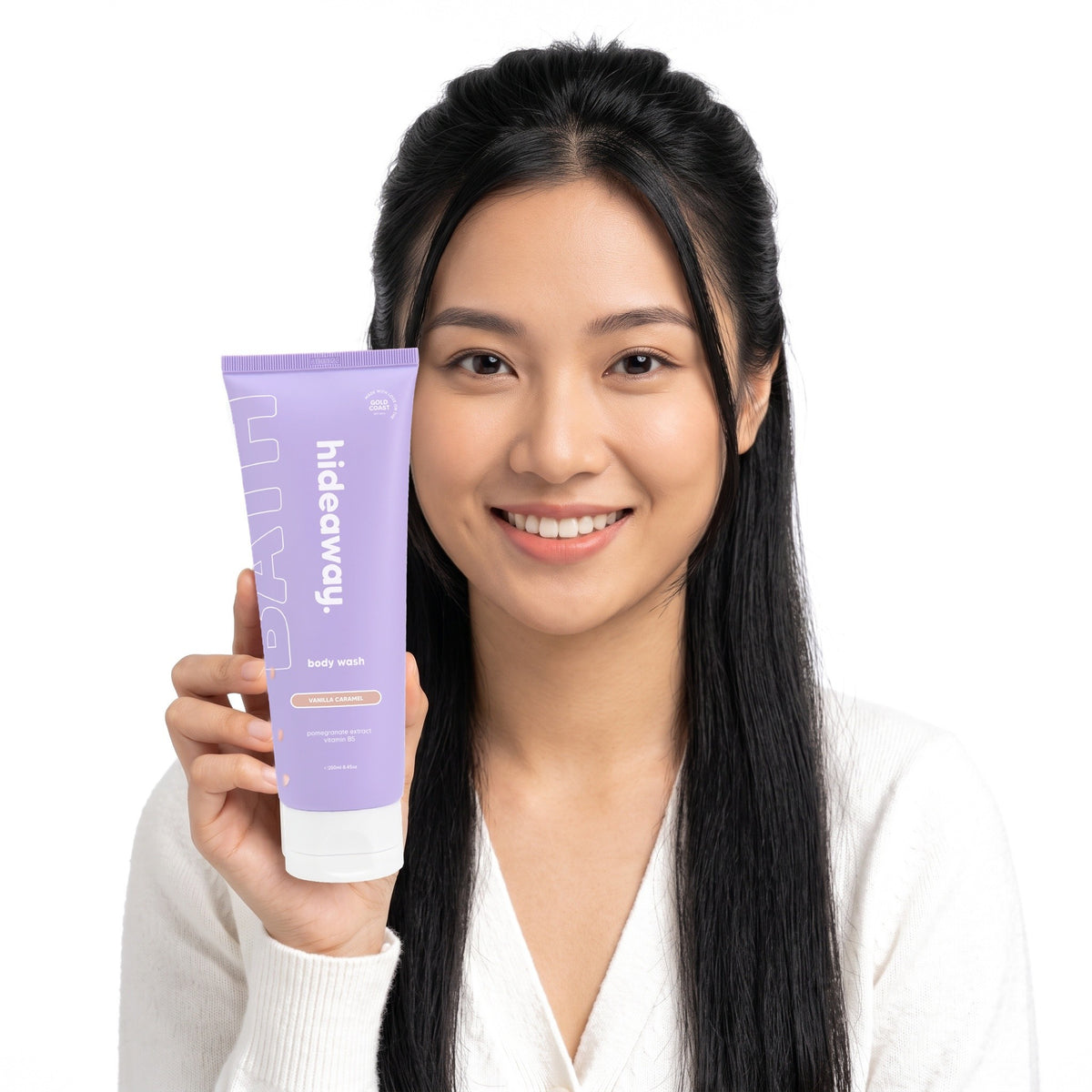 A smiling woman holding Hideaway. Vanilla Caramel body wash